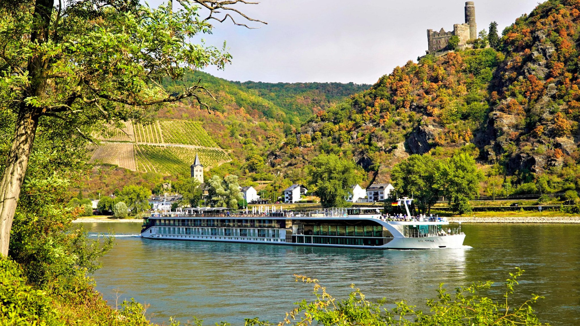 An AmaWaterways river ship sailing the Rhine beneath a hilltop castle and terraced vineyards.