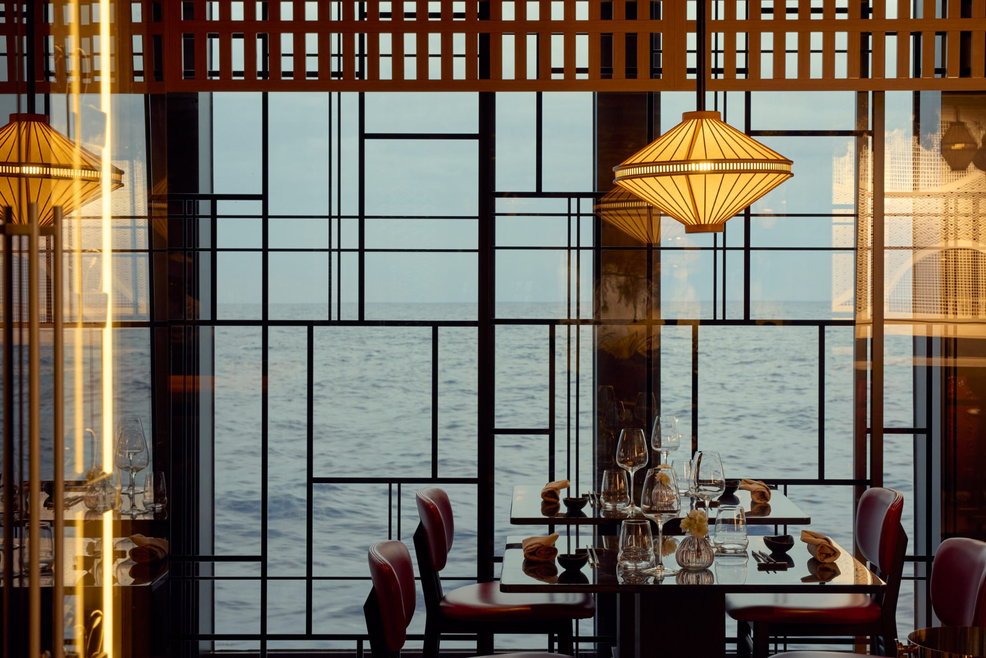 A lantern-lit restaurant table aboard an Explora Journeys ship, with floor-to-ceiling windows framing the open sea.